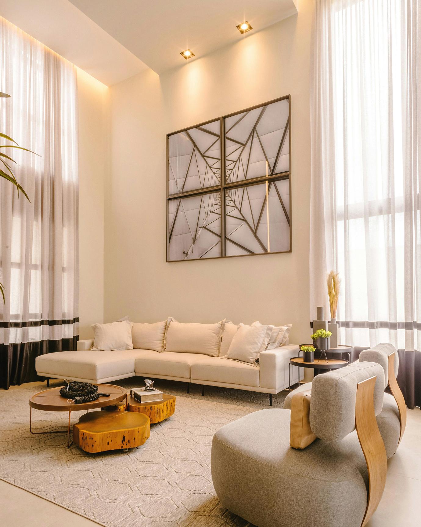 Ein modernes Wohnzimmer mit einem beigefarbenen Ecksofa, großen Fenstern, einem quadratischen Bild an der Wand und zwei runden Couchtischen.
