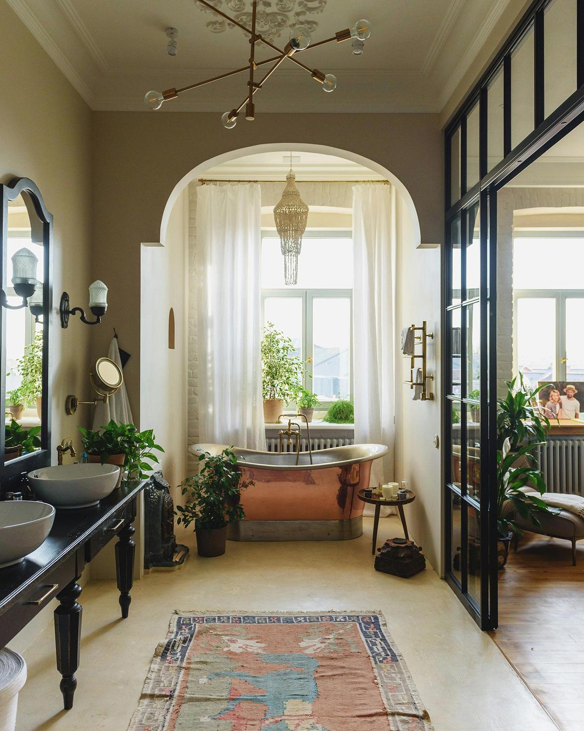 Ein luxuriöses Badezimmer mit einer freistehenden Badewanne aus Kupfer, einem verzierten Teppich und Pflanzen.